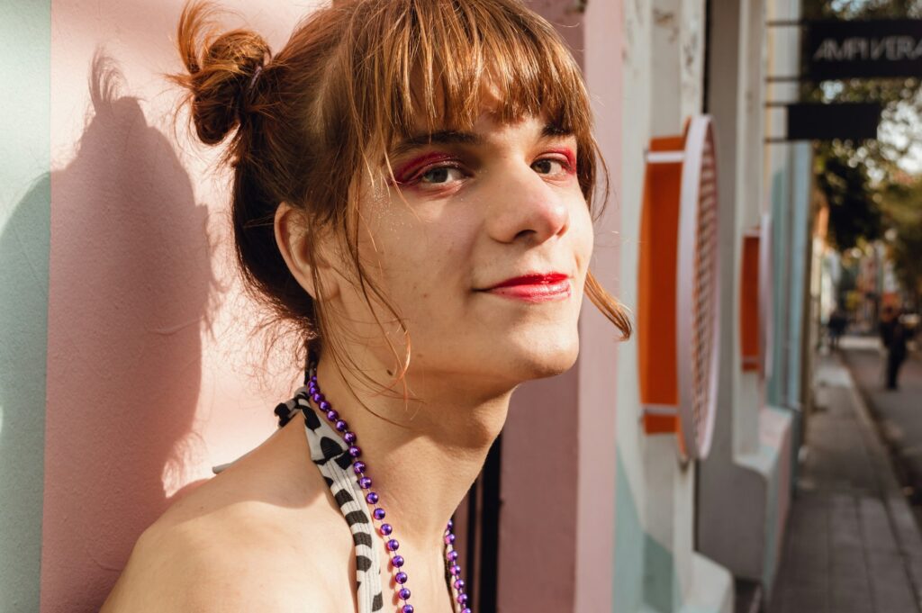portrait of a smiling young transgender woman leaning against a wall in the street