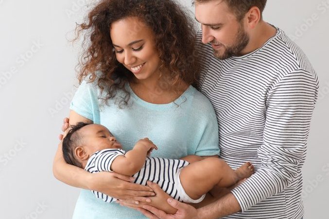 Coppia sorridente che tiene tra le braccia il loro neonato, rappresentando la transizione alla genitorialità.